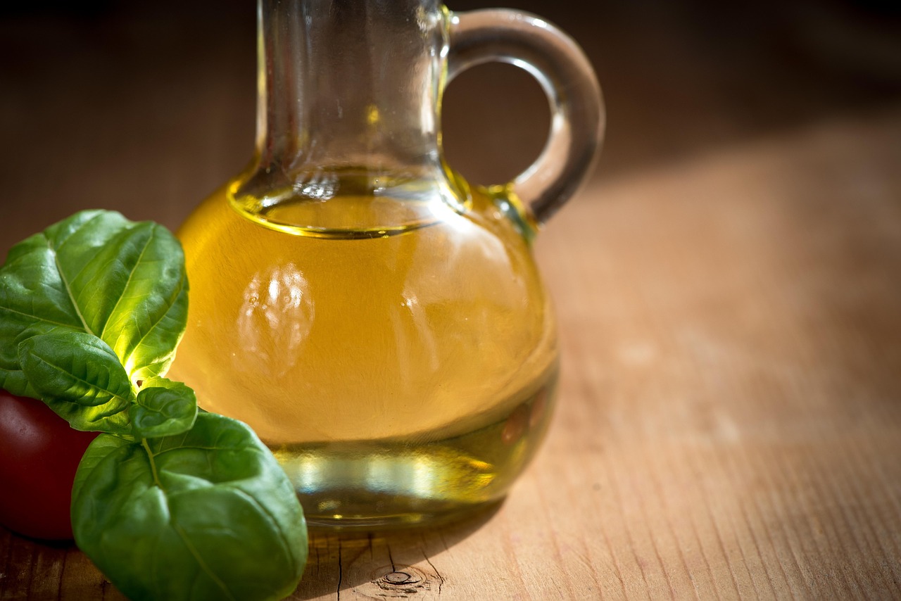 Des bouteilles d'huile d'olive en verre entourées de tomates et de feuilles de basilic
